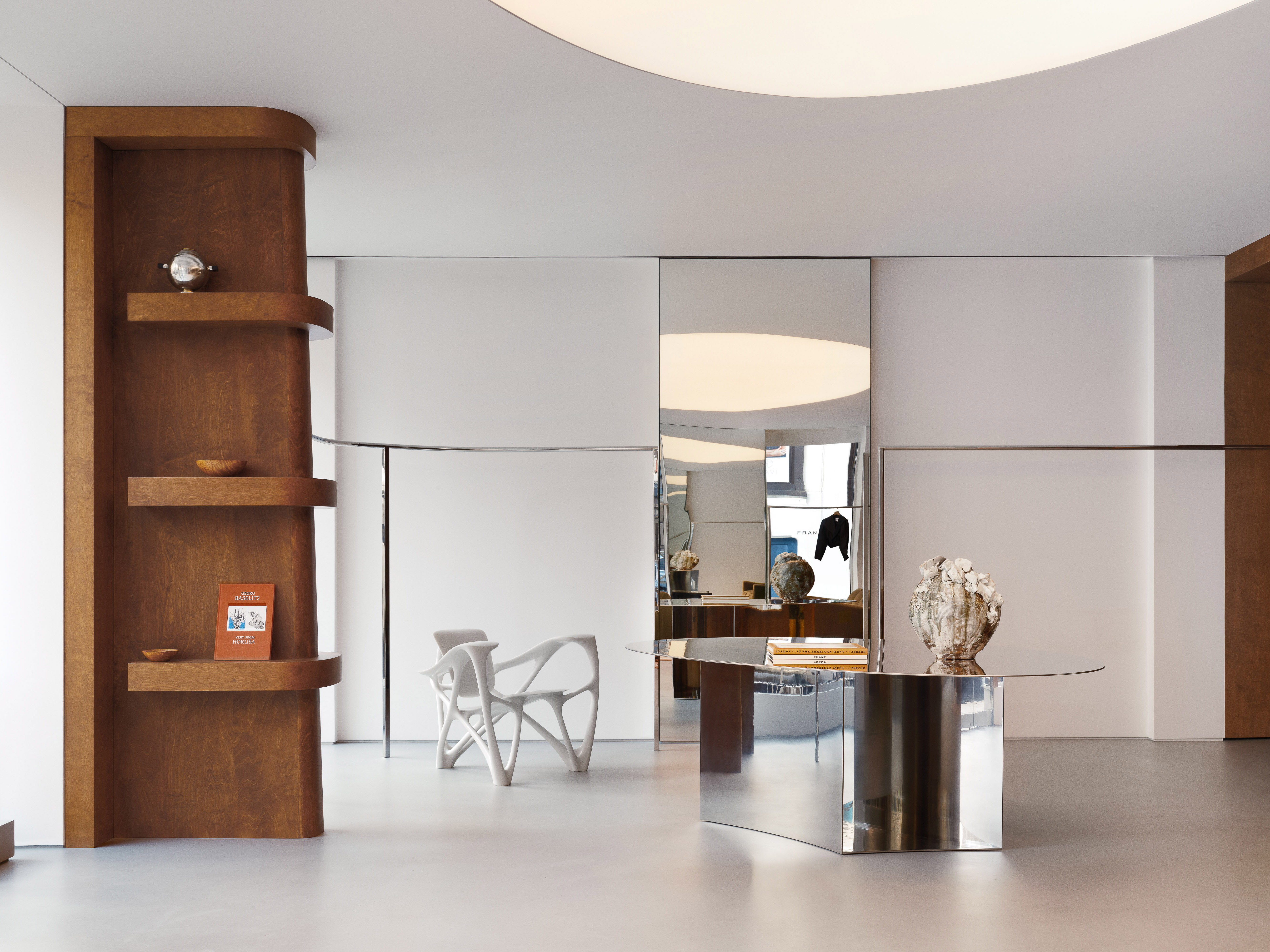 Minimalist interior with sculptural chair, metal table with vases, and wood shelving, creating a modern and elegant space.
