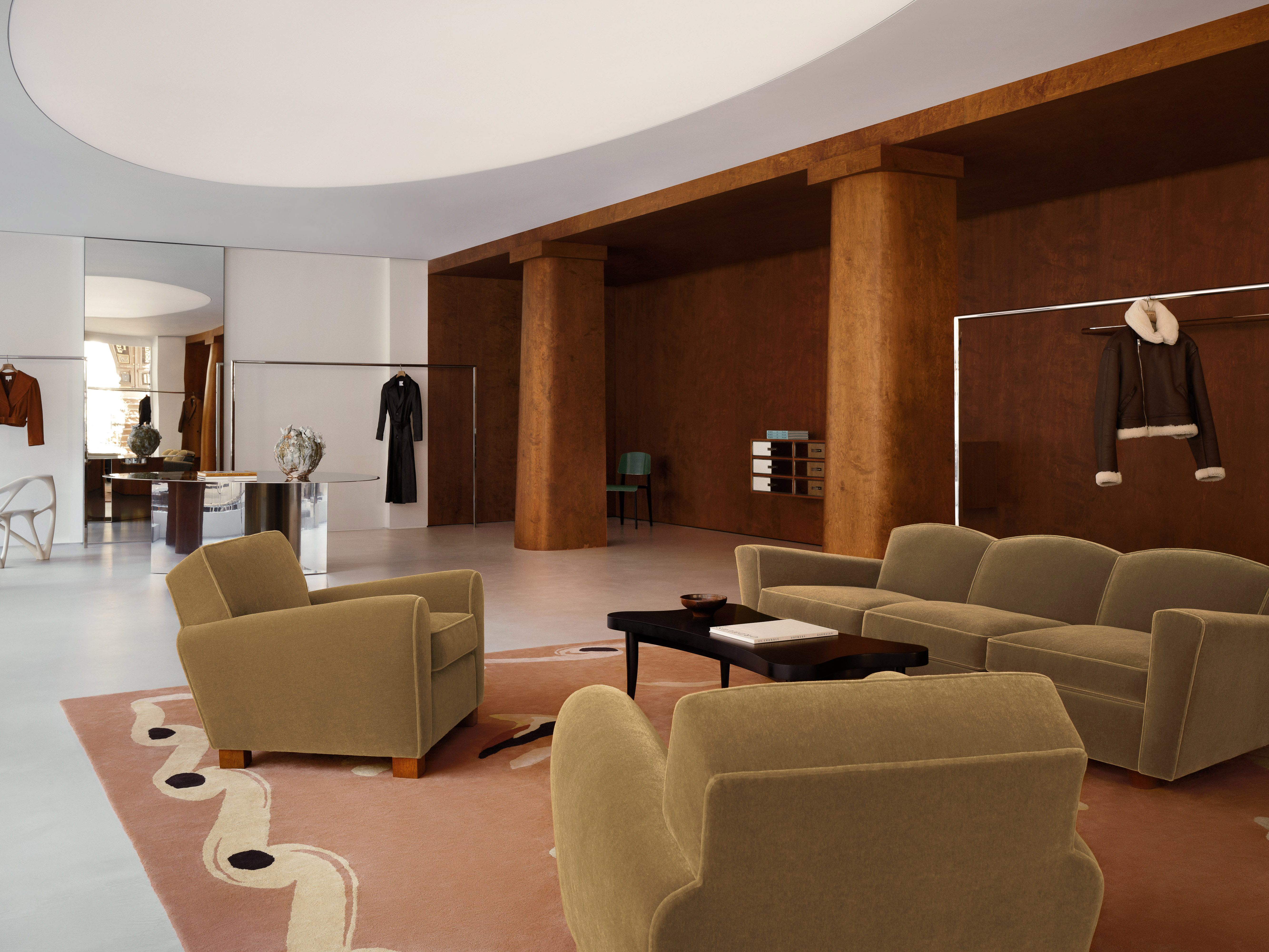 Interior design of a showroom featuring a seating area with olive-green sofas and chairs, set on an patterned pink and white rug.