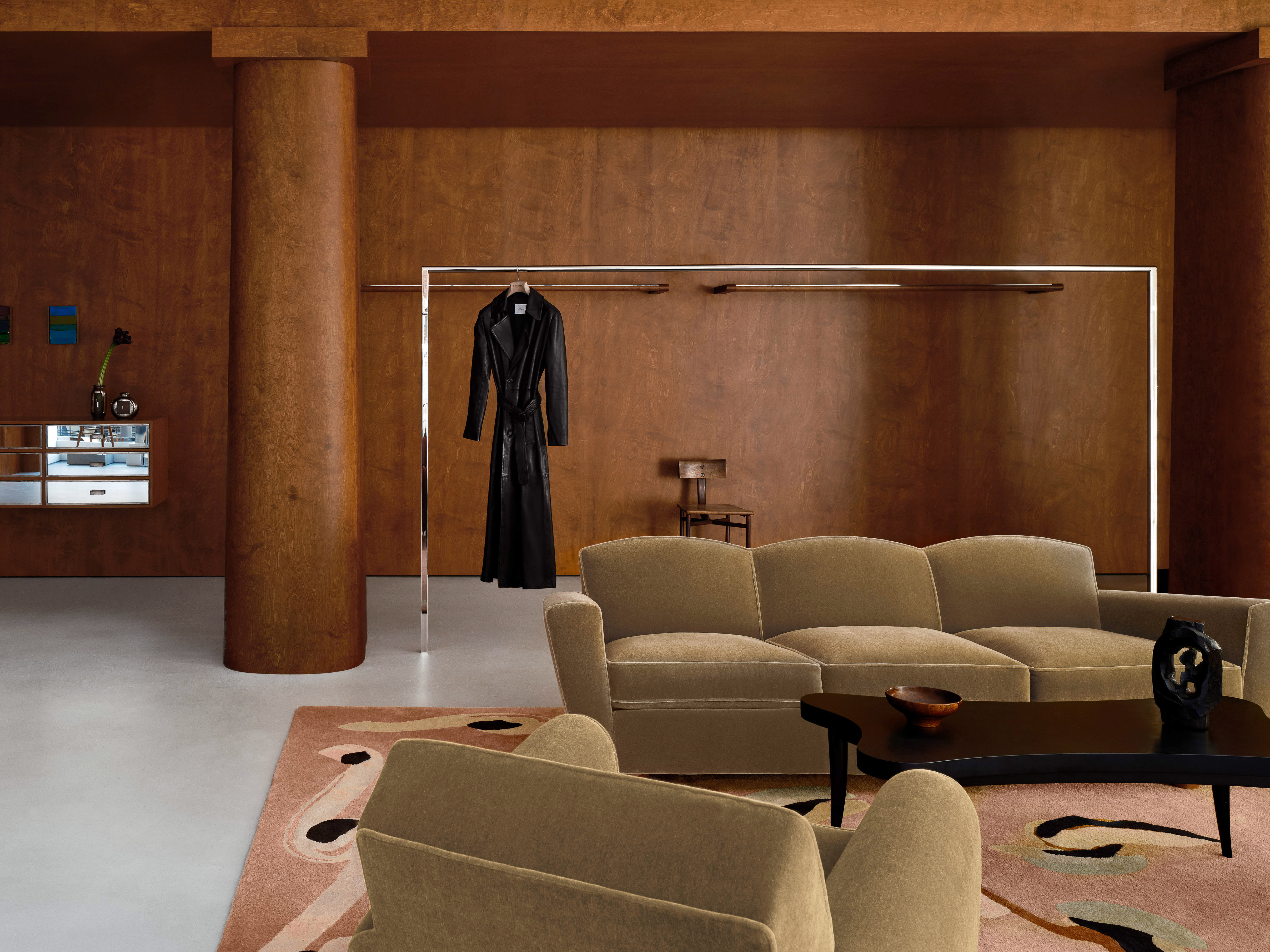 Living room interior featuring a couch, armchair, coffee table, and a dress hanging on a rack in a warm, inviting setting.