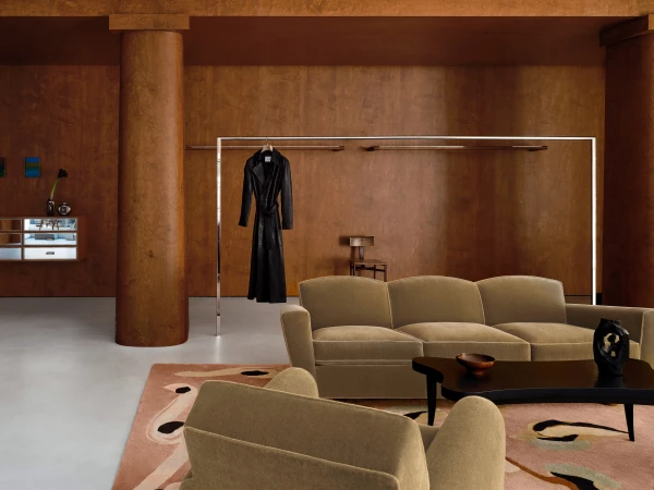 Living room interior featuring a couch, armchair, coffee table, and a dress hanging on a rack in a warm, inviting setting.