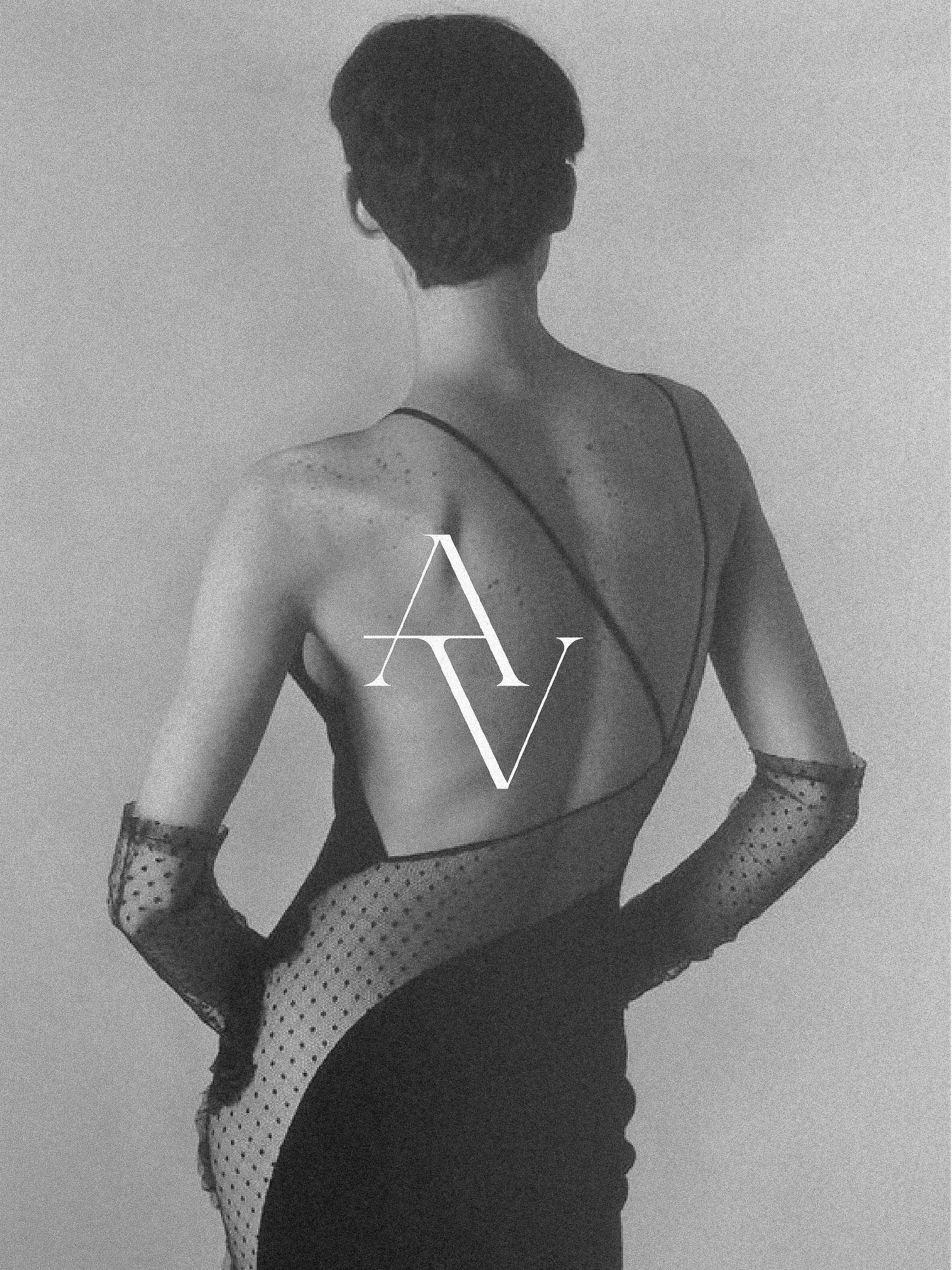 Back view of a fashion model in a black dress and gloves against a neutral background in a studio. The dress has a sheer dotted panel.