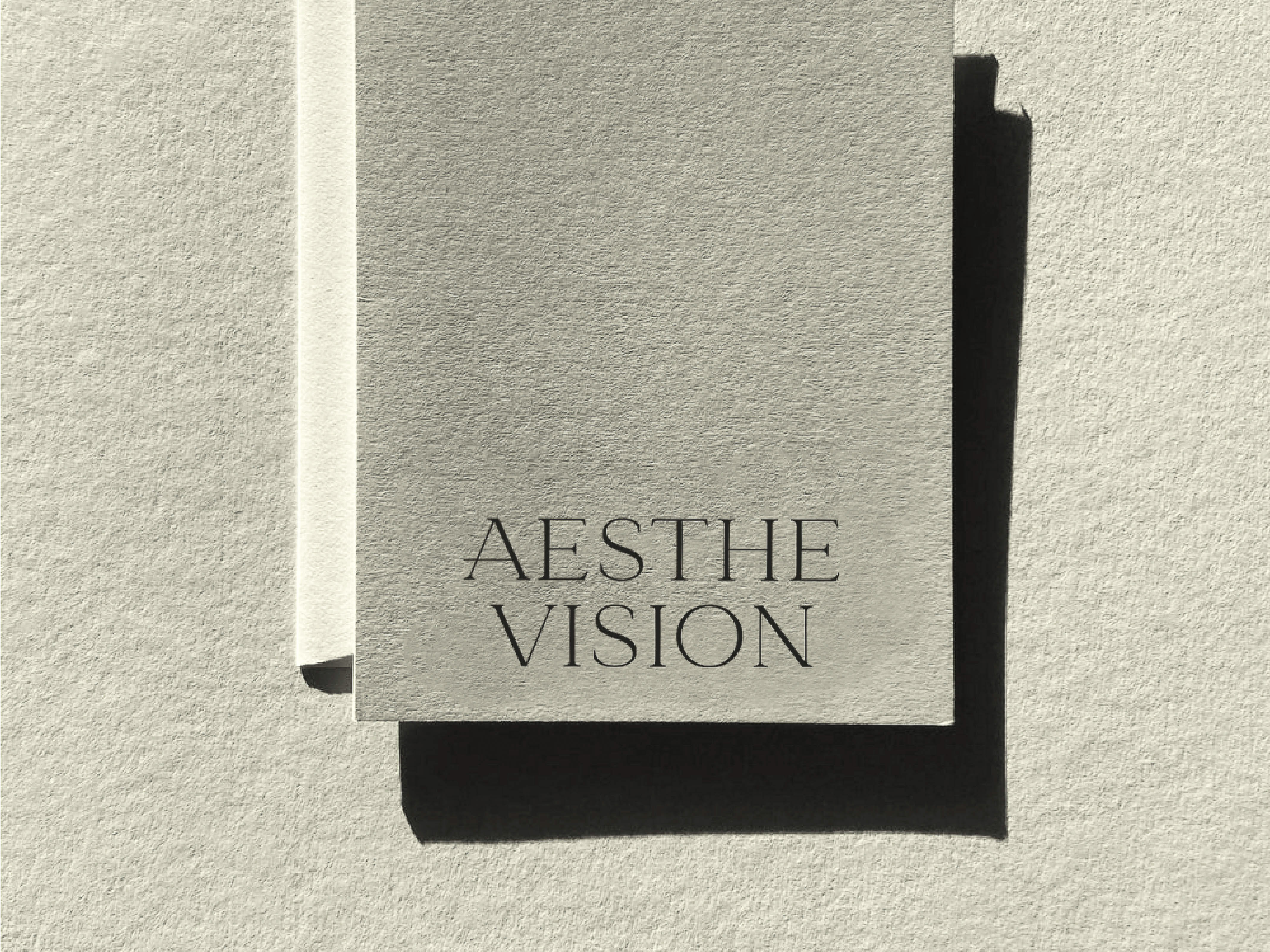 Close-up of two stacked textured cream-colored cards with minimalist dark grey text reading 'Aesthe Vision' in a simple sans-serif font.