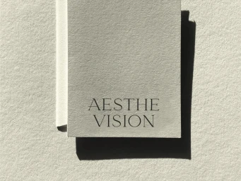 Textured off-white card printed with Aesthevision typography casting a sharp dark shadow on textured paper.