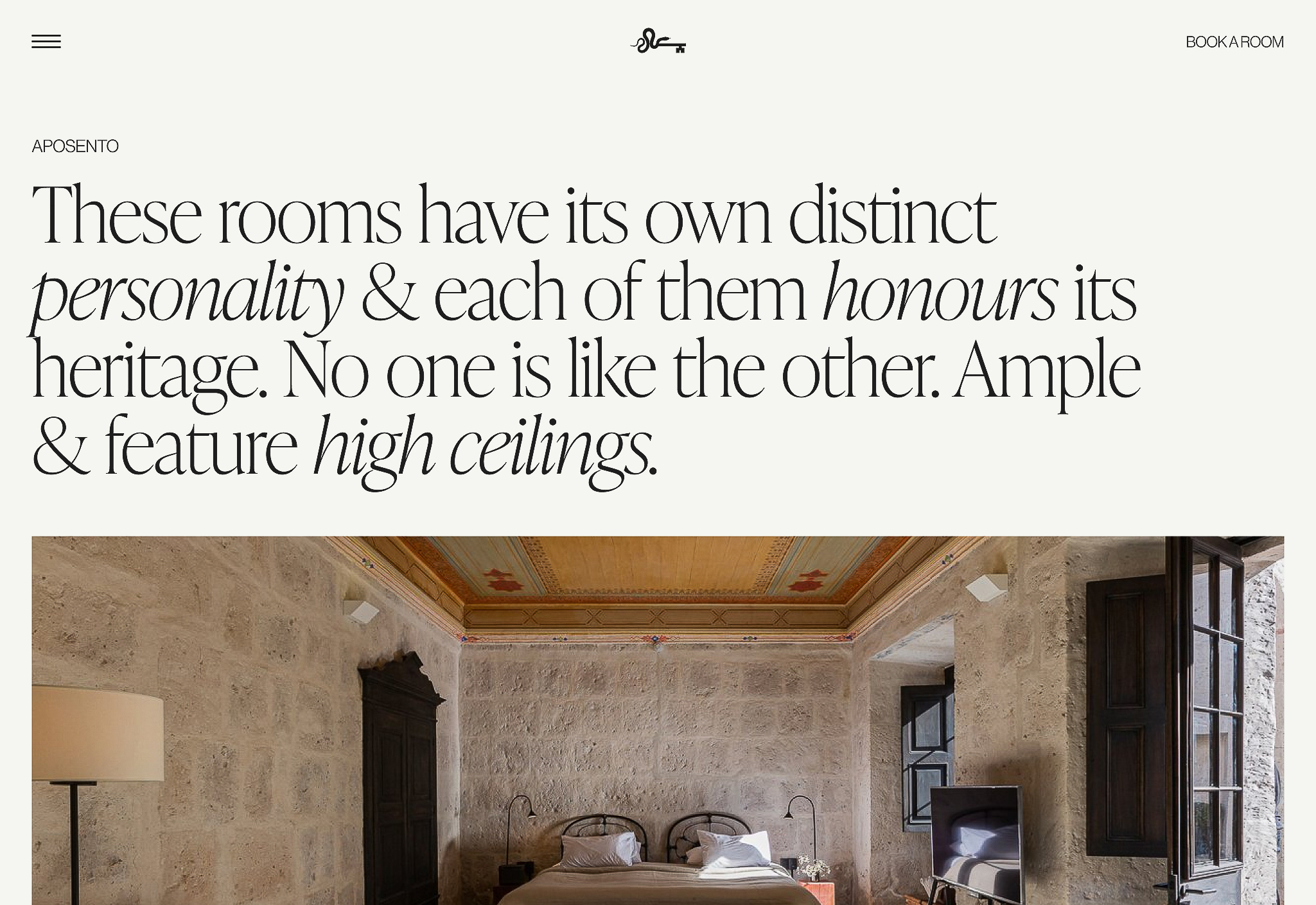 Interior of a bedroom with textured walls, decorative ceiling, large bed, and lamp, with an open door to an adjacent room.