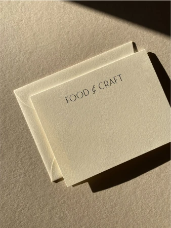 An envelope and card are displayed on a neutral surface, with the text 'FOOD & CRAFT' printed in simple, elegant font.