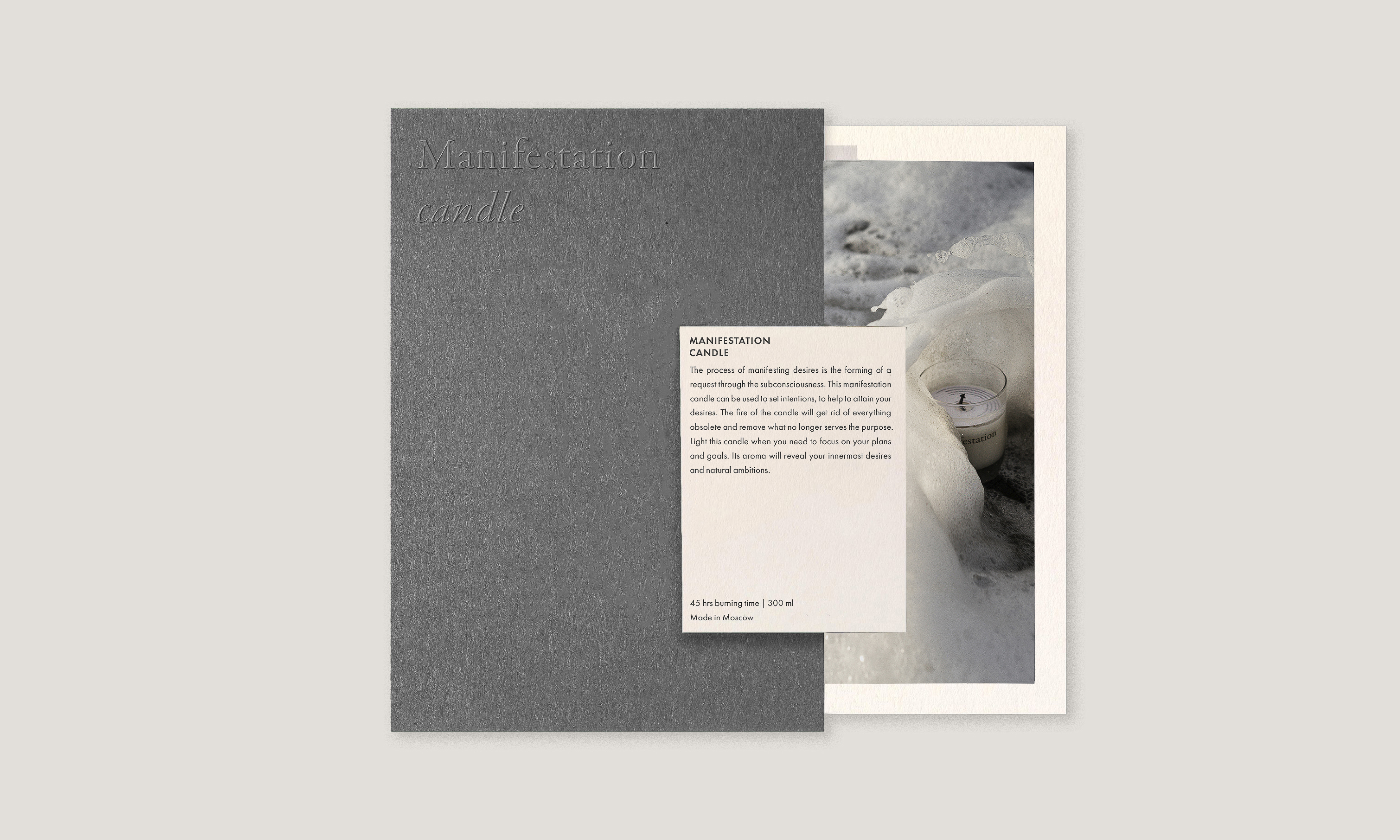 Still life composition featuring a grey 'Manifestation candle' box, a product description card, and a candle amidst a snowy backdrop.
