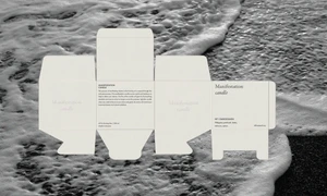 Unfolded off-white candle box packaging dieline laid flat over dark beach sand and foaming white ocean water.
