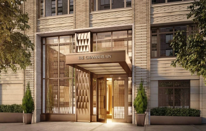 Exterior of The Chamberlain building with a patterned entrance, potted evergreen plants, and a light brick facade in an urban setting.