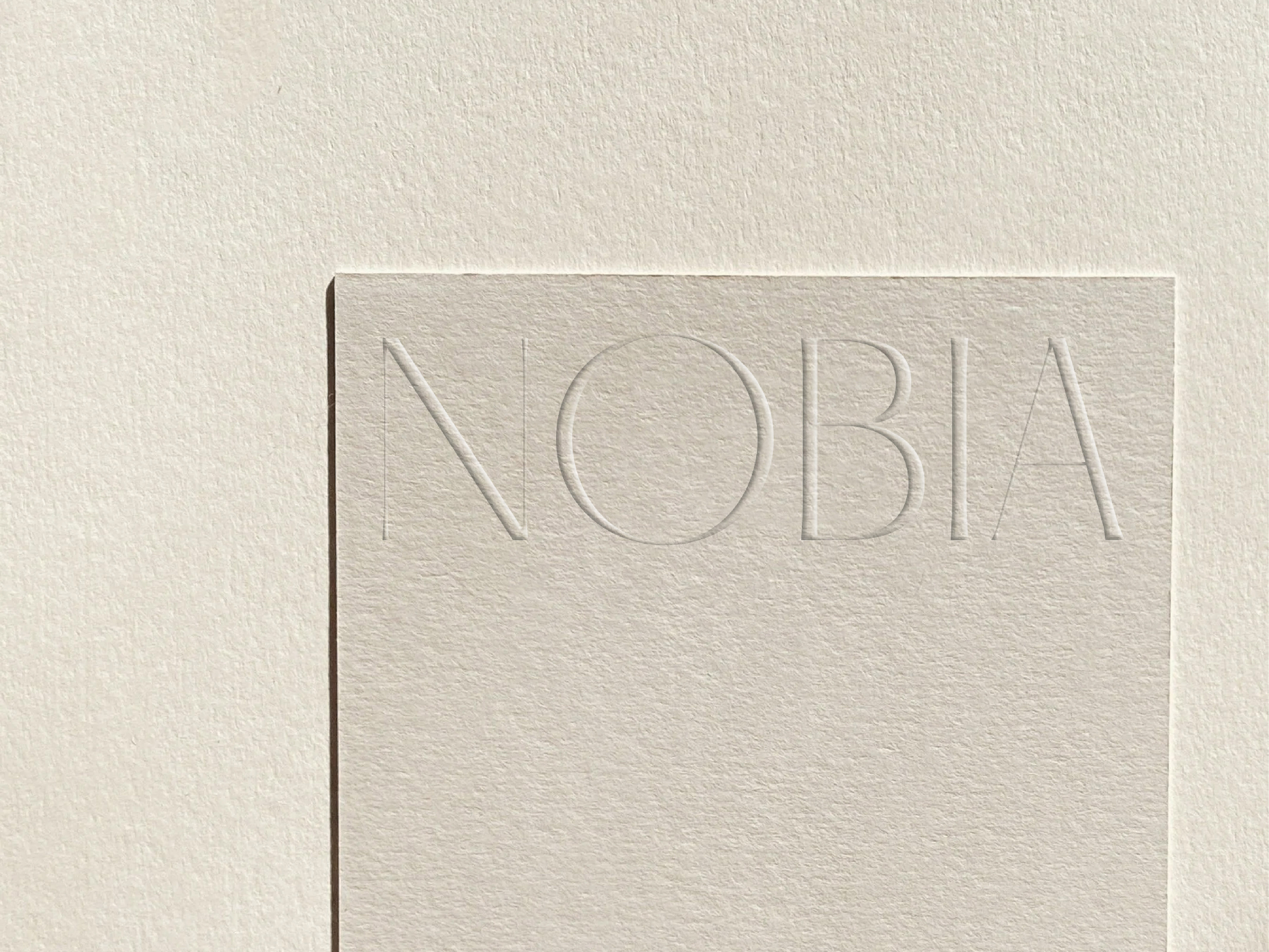 Close-up of a textured, neutral-toned cardstock with the word 'NOBIA' subtly embossed on its surface in simple, sans-serif typography.