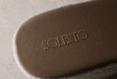 Macro close-up of a brown textured leather insole debossed with the Solento logo, bordered by a light braided jute espadrille trim.