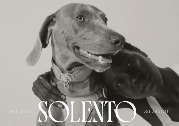 Black woman resting her head against a Weimaraner dog wearing a collar in a monochrome studio portrait for Solento.