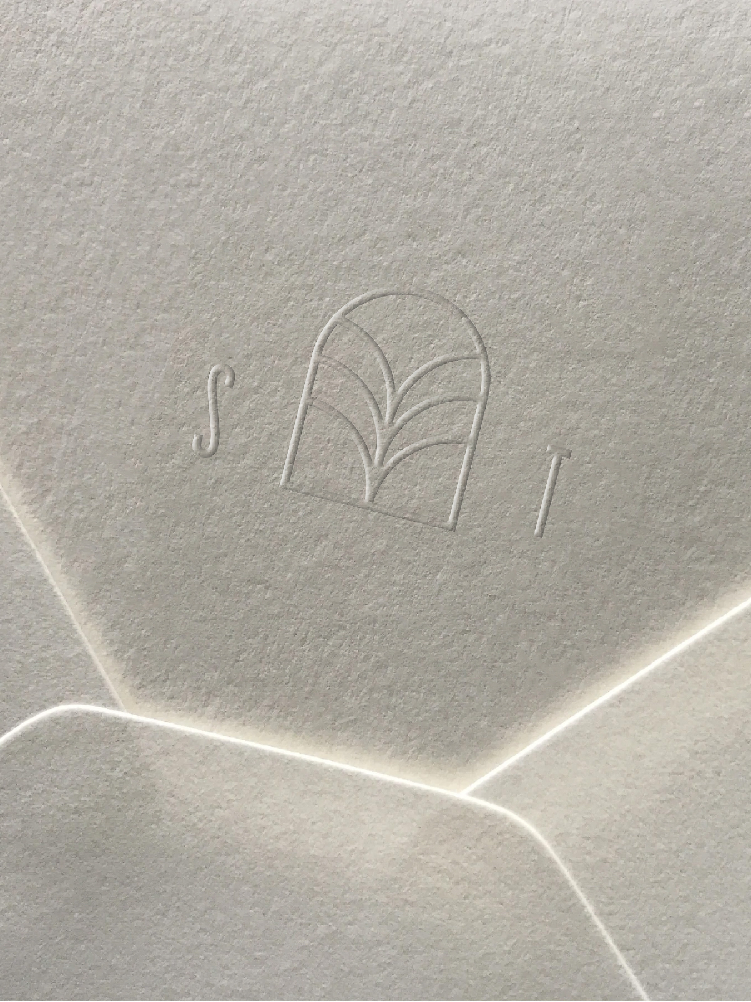 Close-up of an off-white textured paper with an embossed floral logo, showing subtle gradients and natural light.