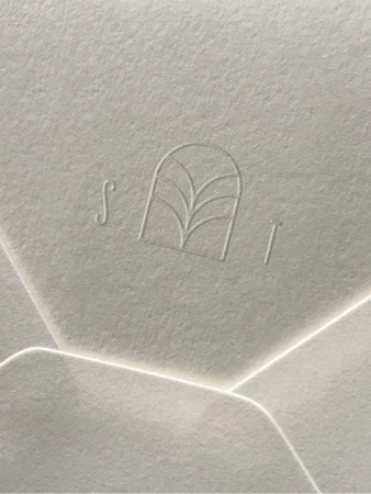Close-up of an off-white textured paper with an embossed floral logo, showing subtle gradients and natural light.