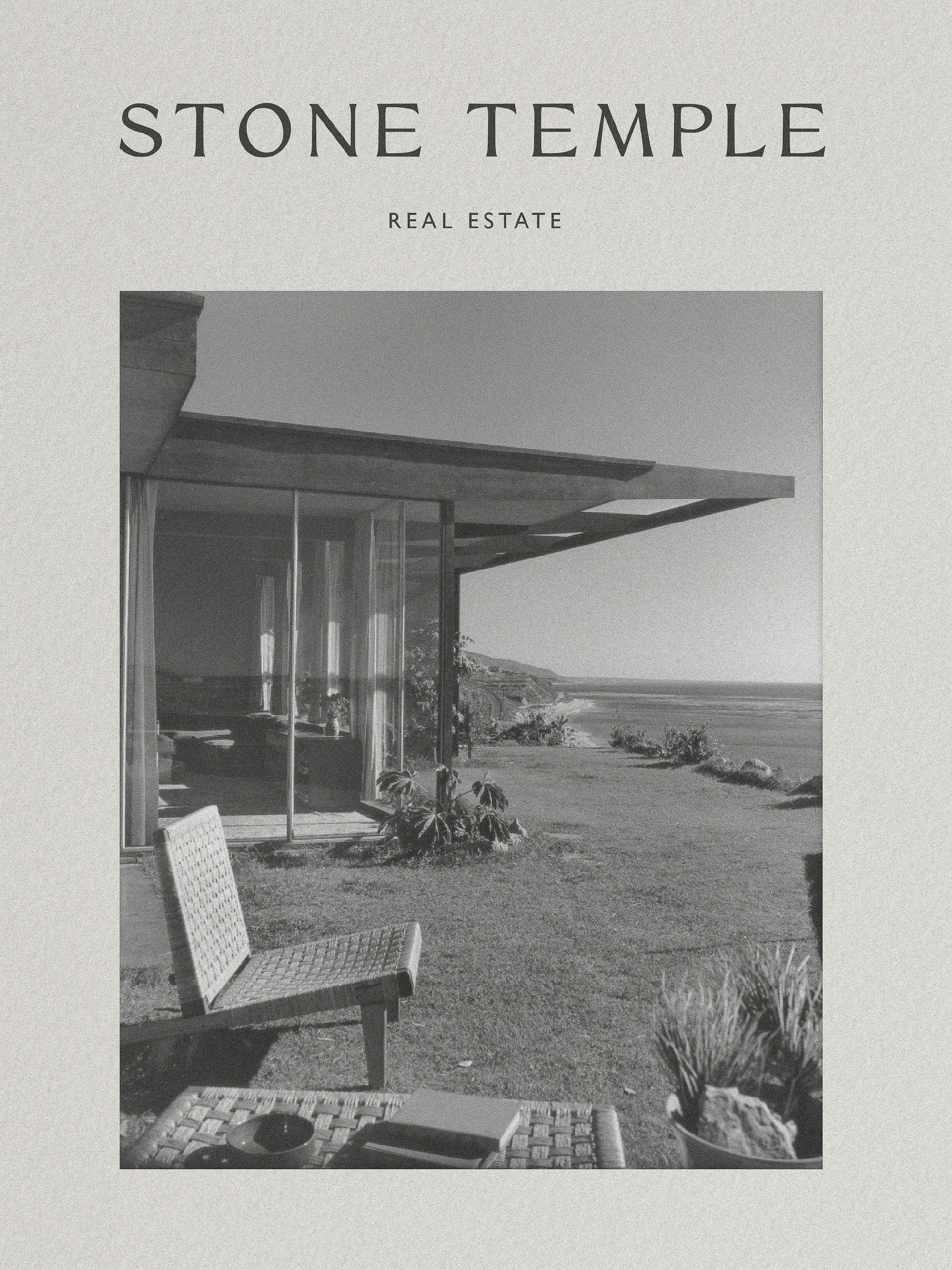 Modernist house with large windows overlooks a grassy yard and the ocean under a clear sky, emphasizing architecture and outdoor living.