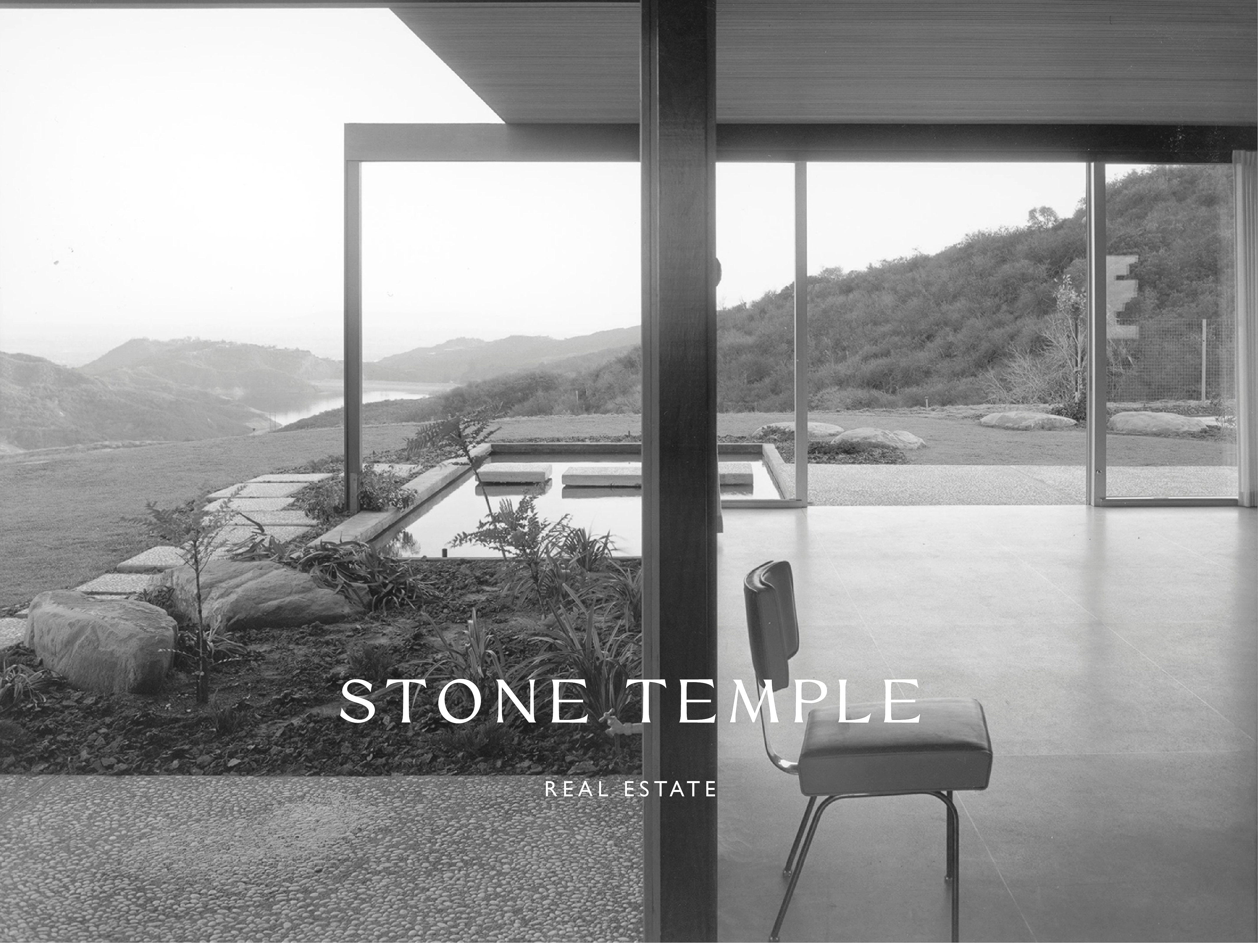Black and white architectural shot featuring a mid-century modern home with views of a lake and mountains through a glass wall.