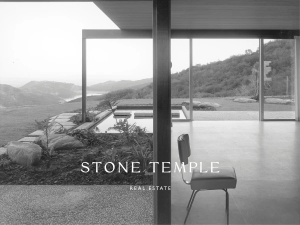 Black and white architectural shot featuring a mid-century modern home with views of a lake and mountains through a glass wall.