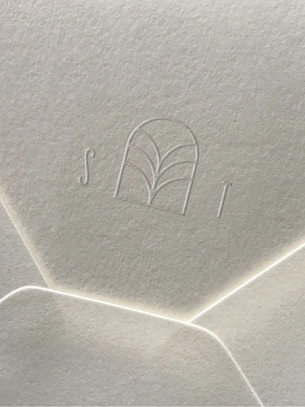 Debossed Stone Temple logo featuring an arch motif and letters S and T on textured cream paper envelope flap.