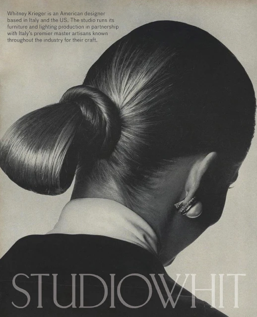 Monochrome studio shot of woman with elegant updo and statement earrings facing away; neutral backdrop, stylish and sophisticated visual.