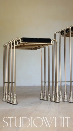 Two-tiered gold metal side table set with modern design, textured metallic legs, and black top, on a neutral background.