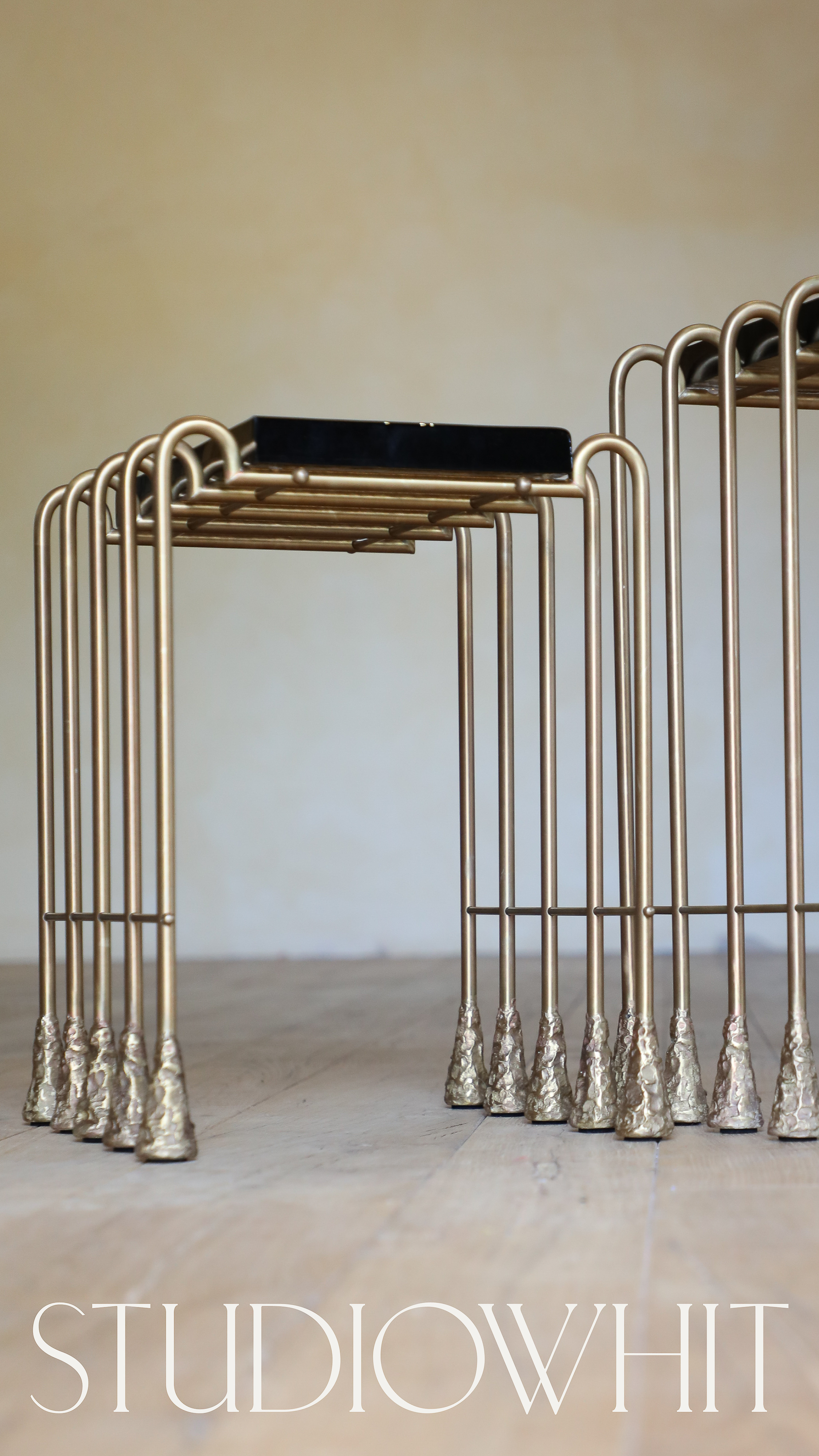Two gold metal side tables with multiple vertical supports and dark-colored tops, set against a neutral wall, with the word 'STUDIOWHIT' at the bottom.
