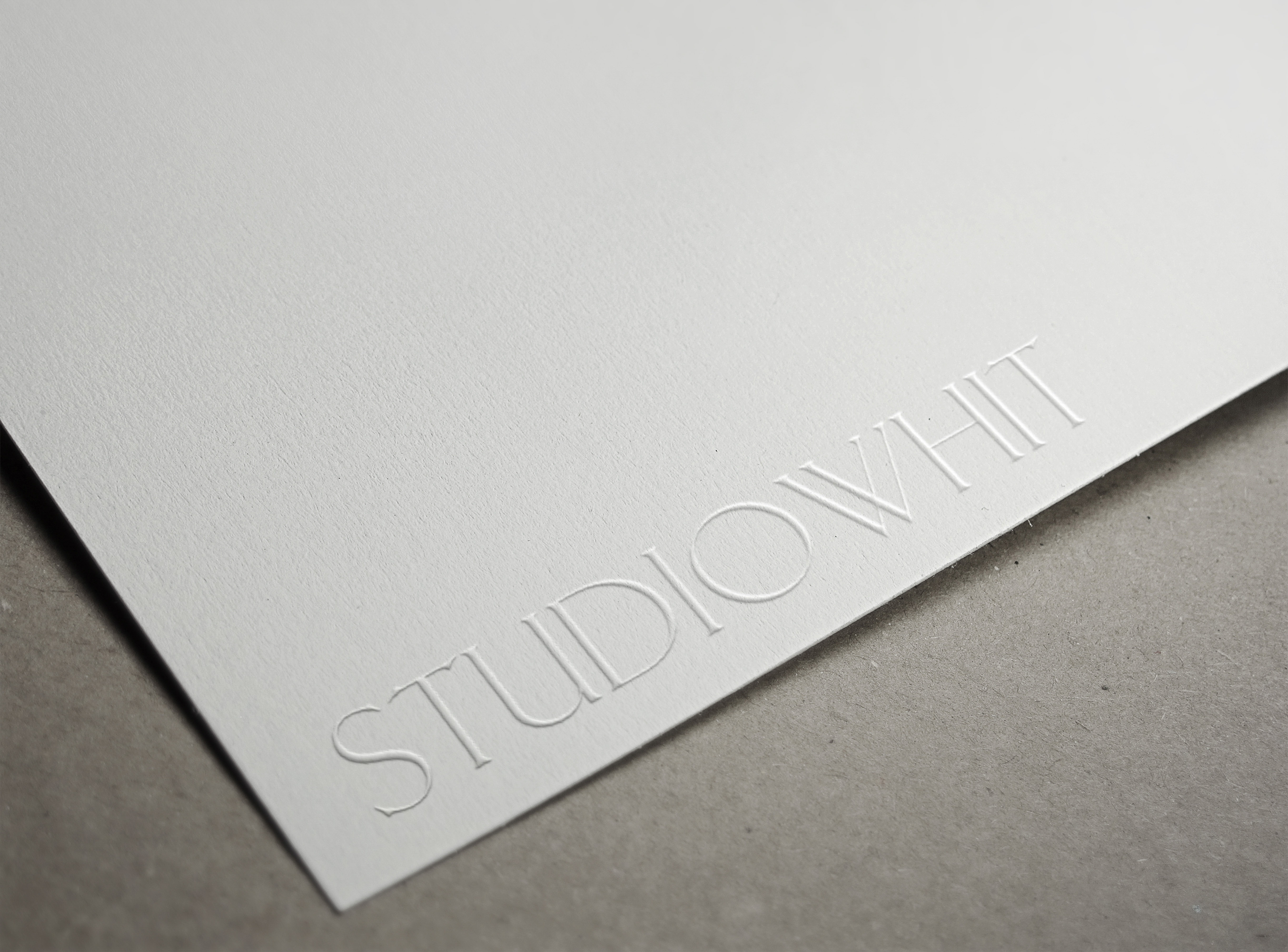 Close-up of embossed studio logo on textured white paper with a gray background, creating a minimalist and elegant presentation.