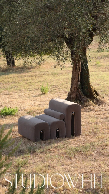 Brown modular sofa sits on grass in front of tree. Minimalist contemporary furniture design in outdoor setting. Studio Whit logo in foreground.