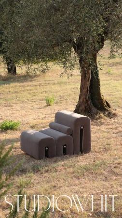 Brown modular sofa sits on grass in front of tree. Minimalist contemporary furniture design in outdoor setting. Studio Whit logo in foreground.