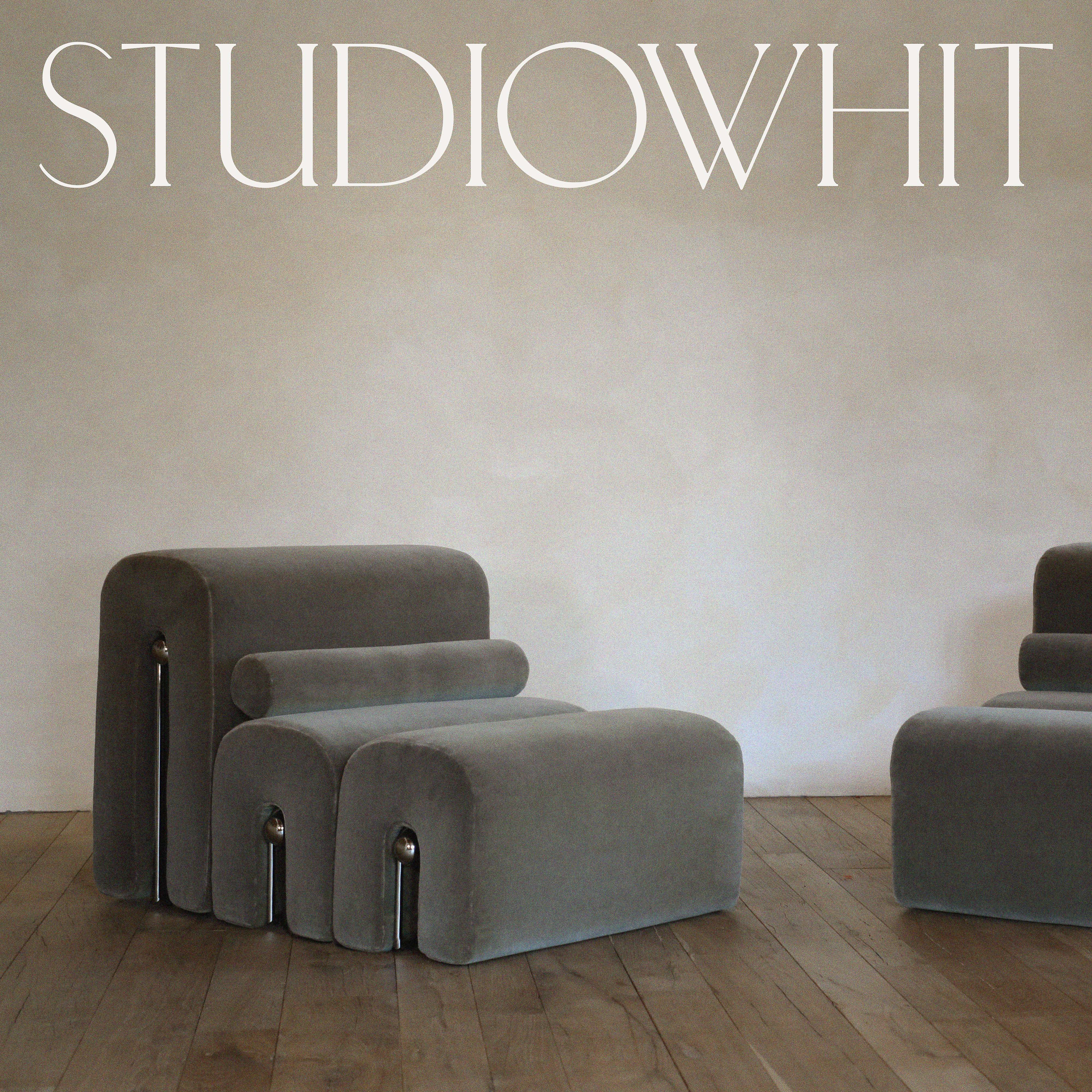 Interior photo of gray lounge chairs with metal accents on a hardwood floor against a light gray wall, showcasing minimalist furniture design.