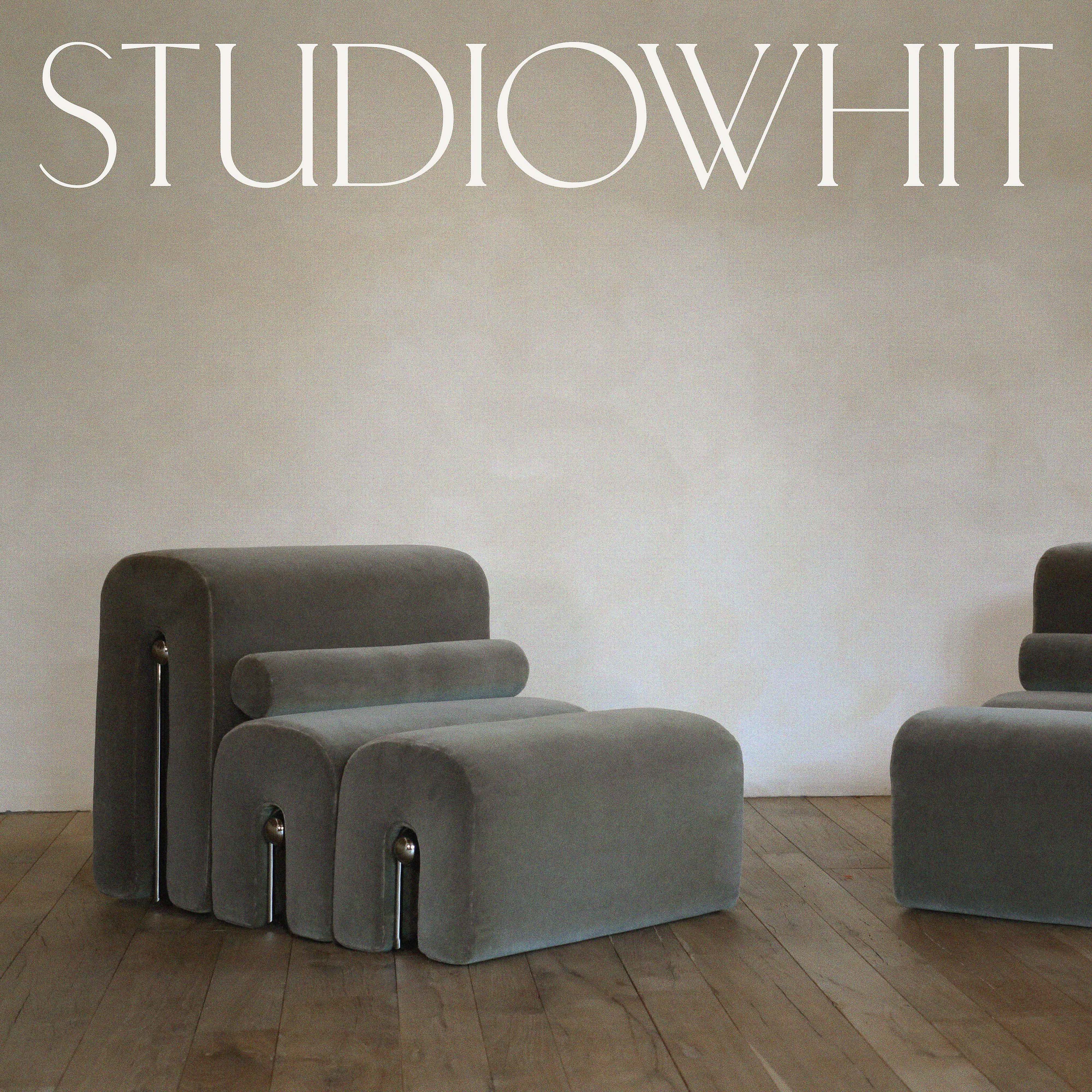 Two gray velvet modular lounge chairs and ottomans on a wood floor against an off-white wall provide modern interior design appeal.