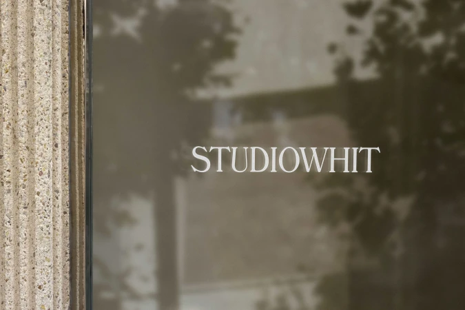 Exterior shot of the Studio Whit building featuring a textured stone column and the company name visible on a reflective window surface.