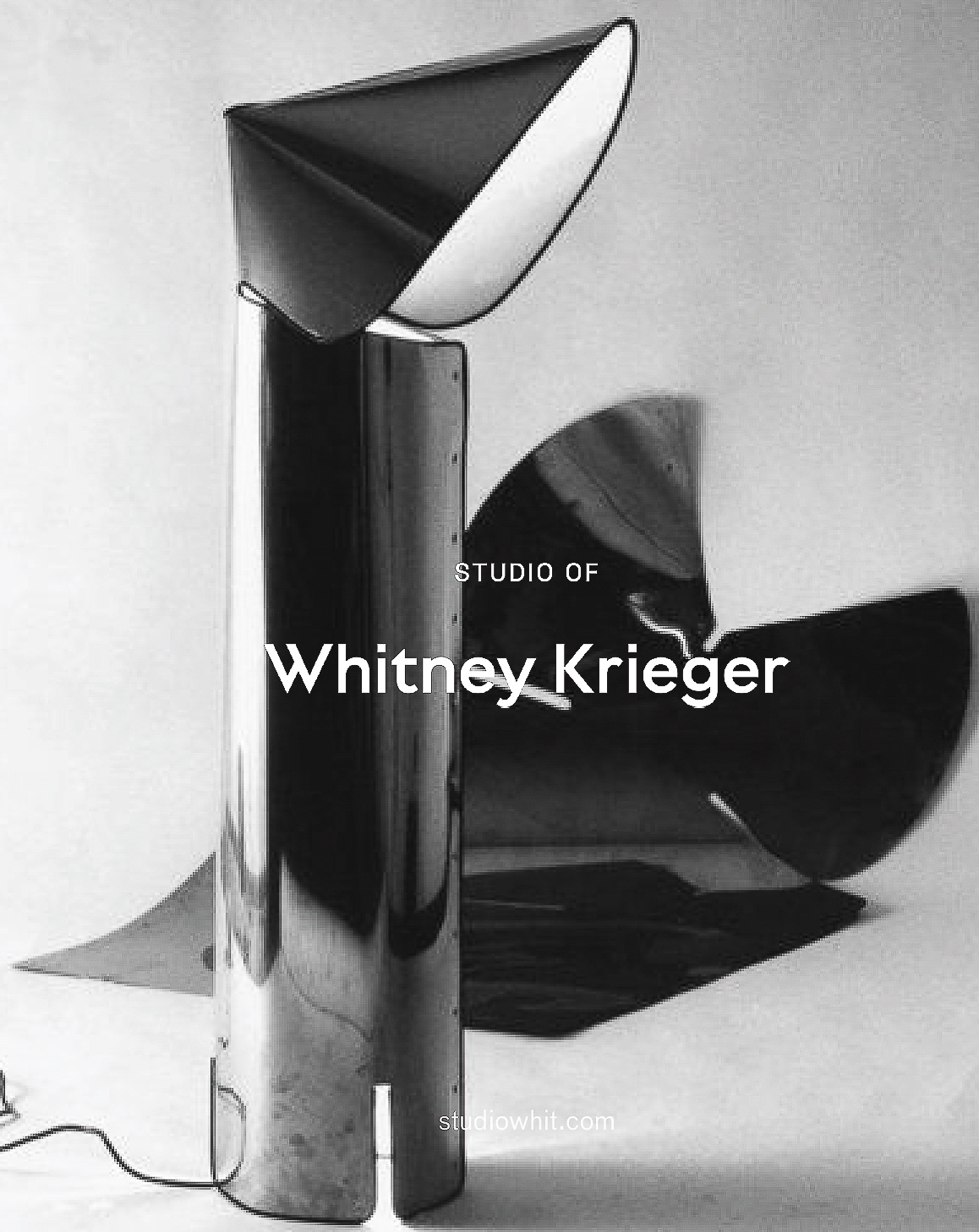 Modern chrome floor lamp with a cone-shaped shade reflecting light in a photo studio, black and white minimalist design.