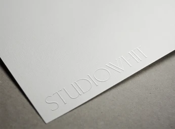 Close-up of white paper featuring an embossed Studio Whit serif logo against a neutral grey surface.