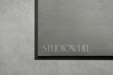 Close-up of embossed Studio Whit logo lettering in white serif typography on dark grey textured paper stationery.