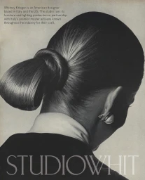Close-up from behind of a woman with a sleek looped ponytail hairstyle, wearing a dark jacket, white collar, and earring.