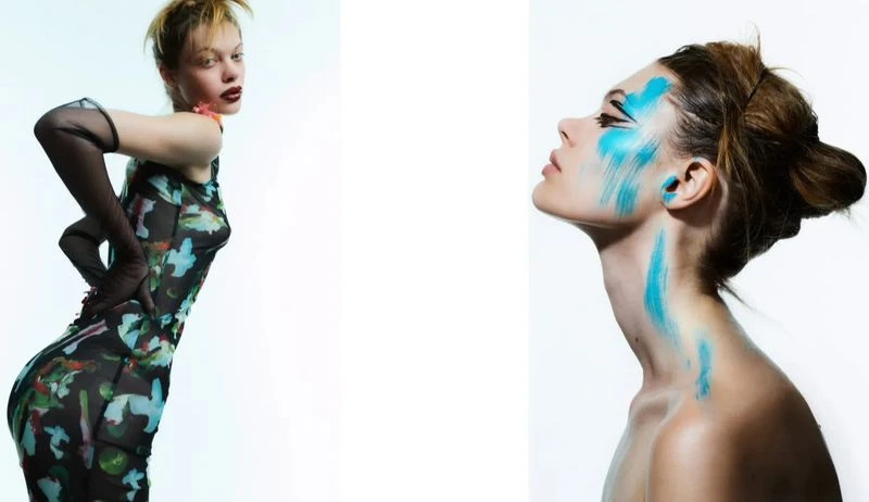 Fashion portrait of a female model with blue makeup, wearing a black printed dress and black gloves against a white backdrop.