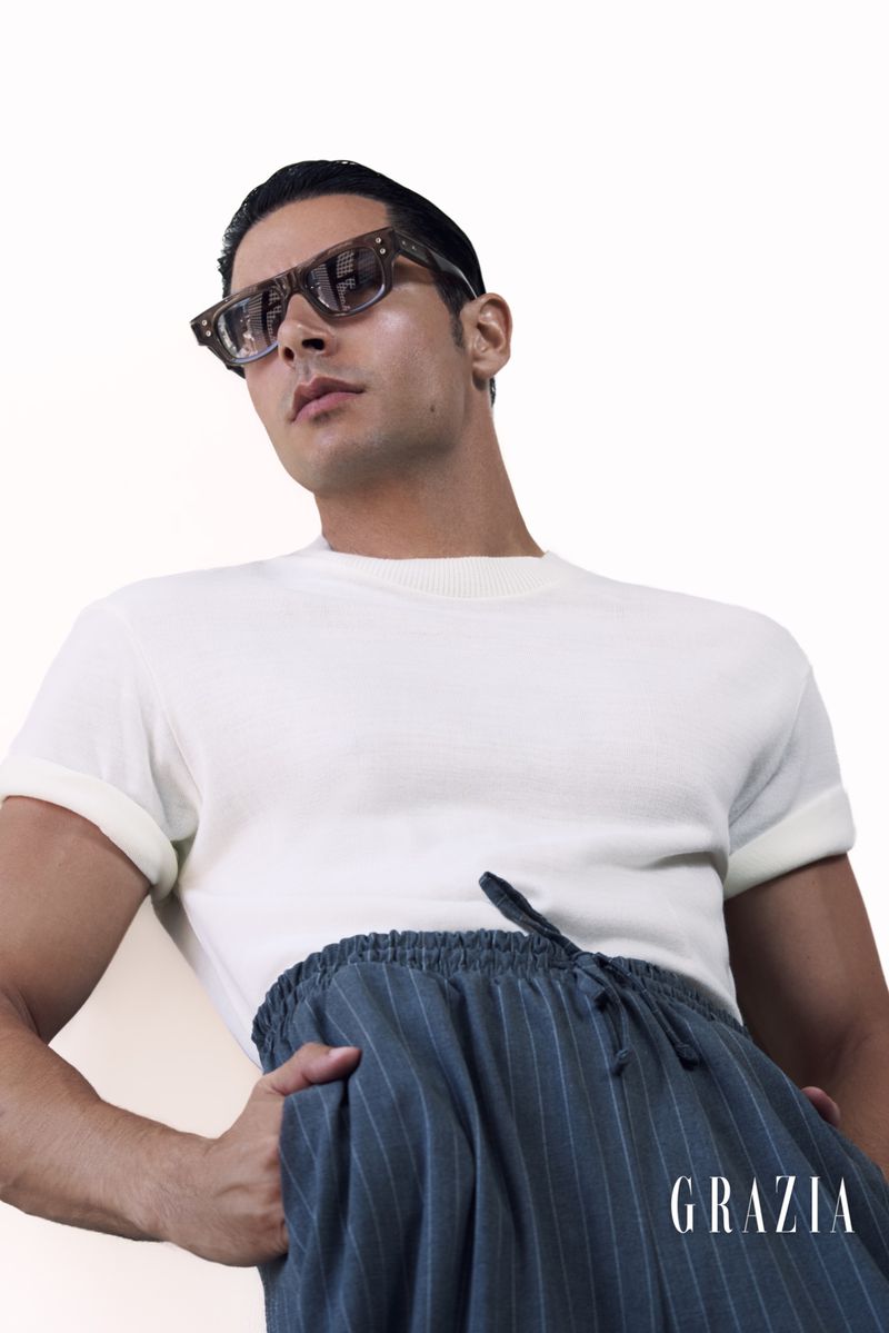 Studio shot of adult male wearing a white t-shirt and blue striped pants with sunglasses, against a clean white background.