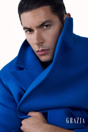 Model Andrea Denver poses in a vibrant royal blue coat with a raised structured collar against a white studio background.