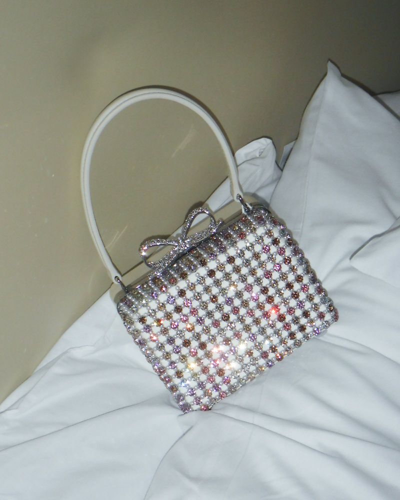Sparkling evening bag with a bow on white bedding, creating a luxurious and elegant fashion statement. Perfect for special occasions.