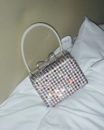 Sparkling evening bag with a bow on white bedding, creating a luxurious and elegant fashion statement. Perfect for special occasions.