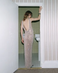 Model Matilda Navratil in a sparkling backless maxi dress posing in a bathroom doorway with green tiles.
