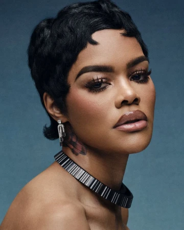 Close-up studio shot of a woman with short black hair wearing a black choker necklace and diamond earrings against a blue background.