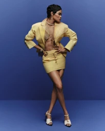 Teyana Taylor wearing a yellow blazer and matching skirt with heeled sandals against a solid blue background for InStyle U.S.