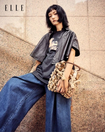 Woman in fashionable dark top and wide-leg jeans poses with a net handbag near a concrete stairway with the magazine ELLE in the corner.