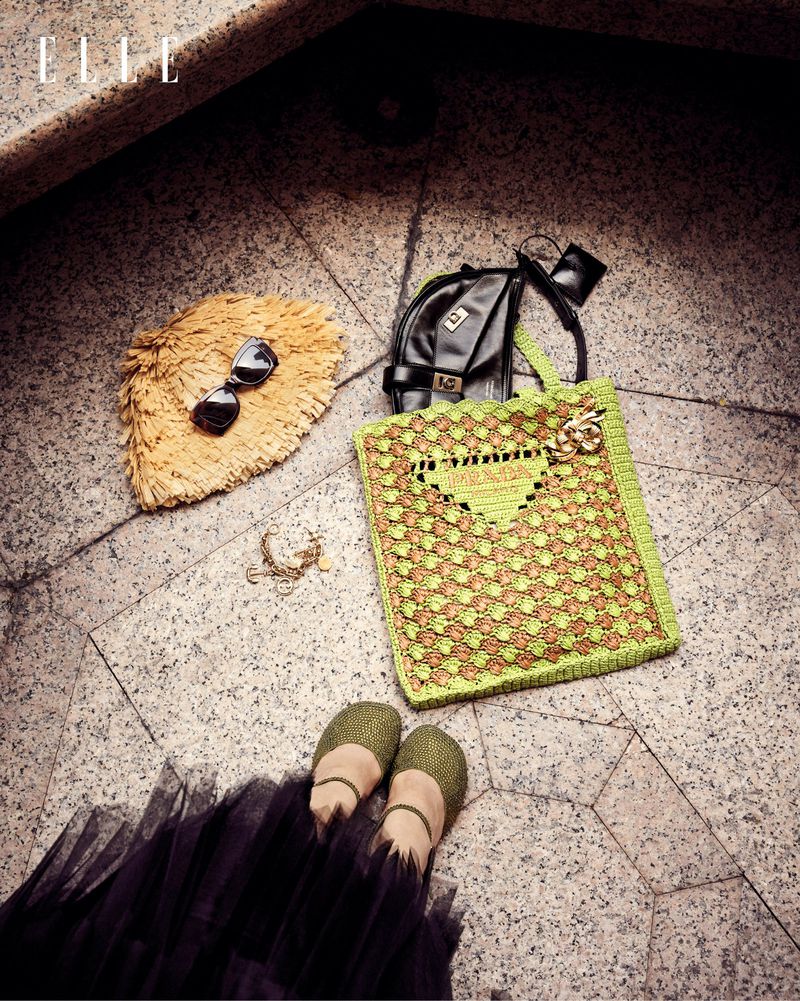 Overhead shot of fashion accessories including straw hat, sunglasses, handbags, jewelry, shoes, and a black tulle skirt on marble stairs.