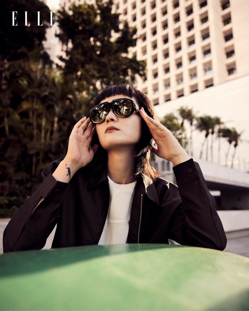 Model Yvette Chau wearing oversized sunglasses and a black jacket in an outdoor urban setting for Elle Hong Kong.