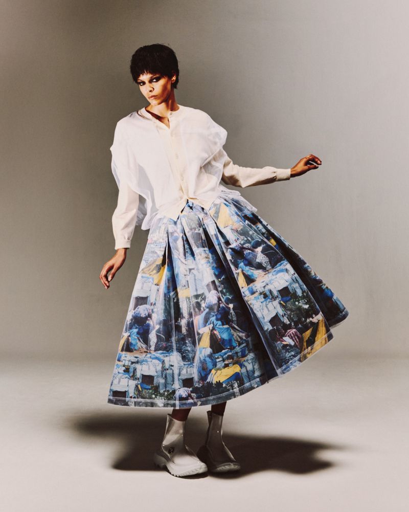 Full-length shot of a woman in a white blouse and printed skirt, posing in a studio with soft lighting and a neutral background.