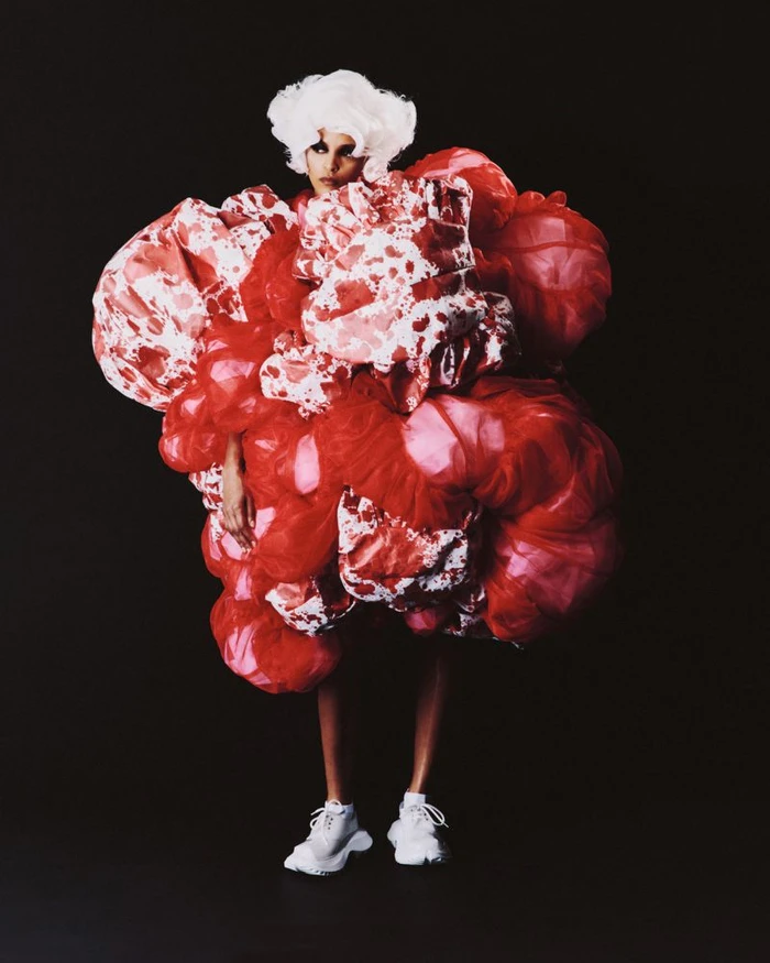 Model Laiza de Moura wearing a voluminous red and white sculptural Comme des Garçons garment against a black background.