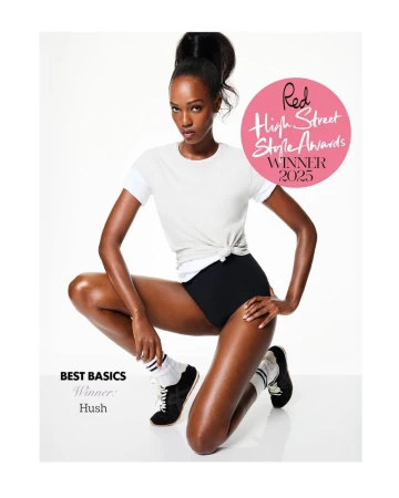 Model Leila Nda posing in a white knotted t-shirt, black briefs, and athletic sneakers against a white studio background.