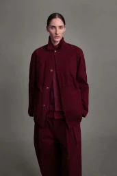 Model wearing a structured burgundy buttoned jacket and trousers against a grey seamless background