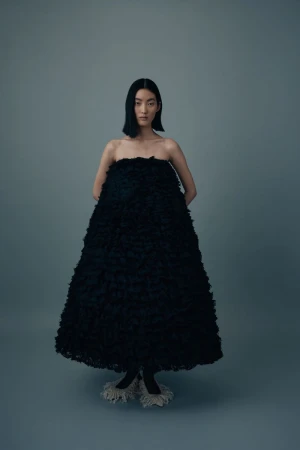 Elegant Asian woman in a large black textured dress posing against a gray backdrop in a fashion editorial studio shot.
